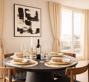 A round dining table set with plates, cutlery, glasses, and a bottle of wine, with a large abstract painting above it.