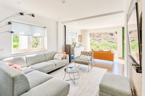 Una sala de estar moderna con un sofá, un sillón y una mesita. Hay un ventanal con vistas a zonas verdes.