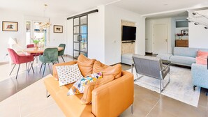 A modern living room with a sofa, chairs, a dining table, and a TV.