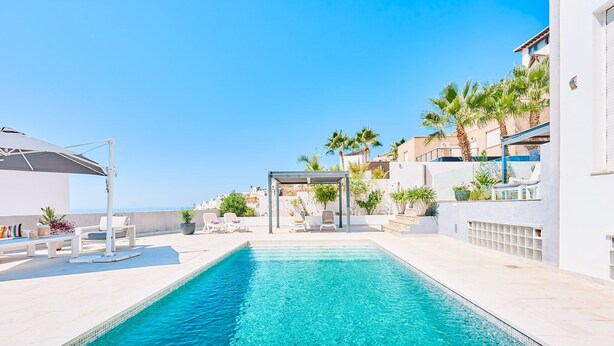 A rooftop pool with lounge chairs, a pergola, and a view of the sea.