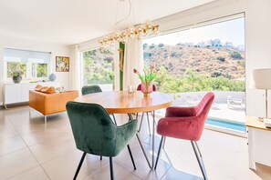 A modern dining area with a round table, two chairs, a sofa, and a view of a pool and hills. - Villa 'La Buena Vida Torrox' with Sea View, Wi-Fi and Air Conditioning (Torrox)