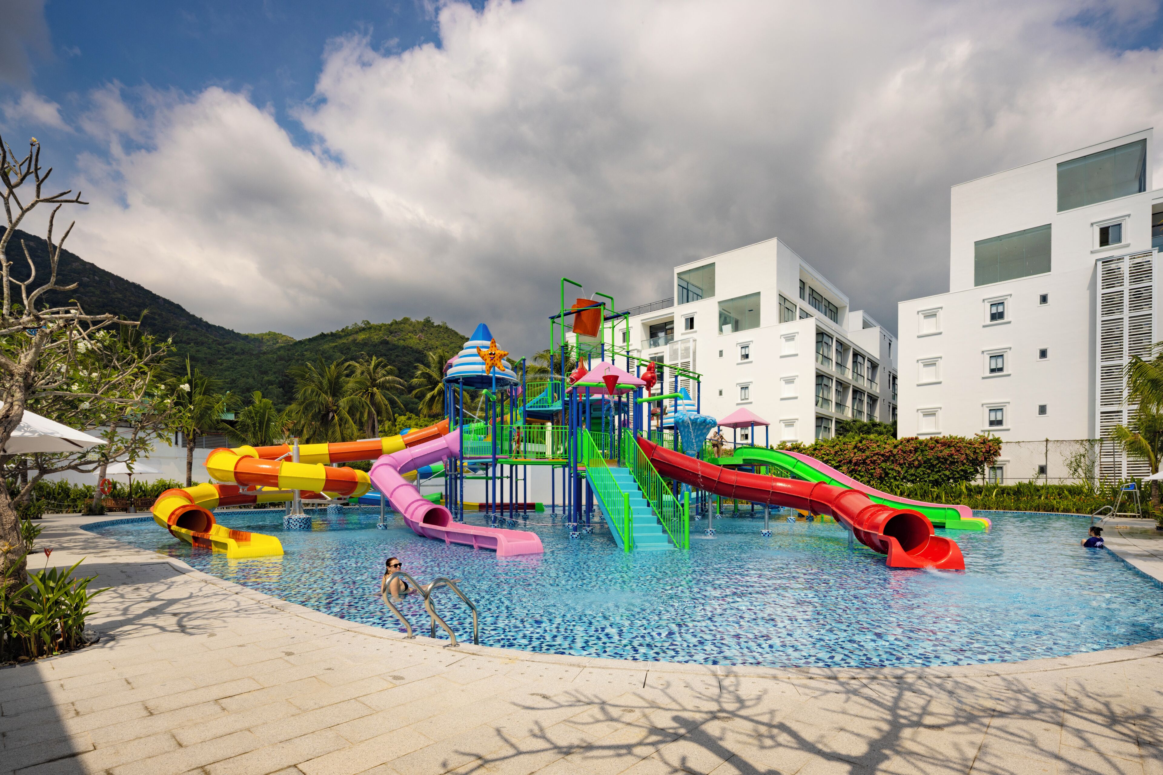 Piscina com toboáguas coloridos e montanhas ao fundo.