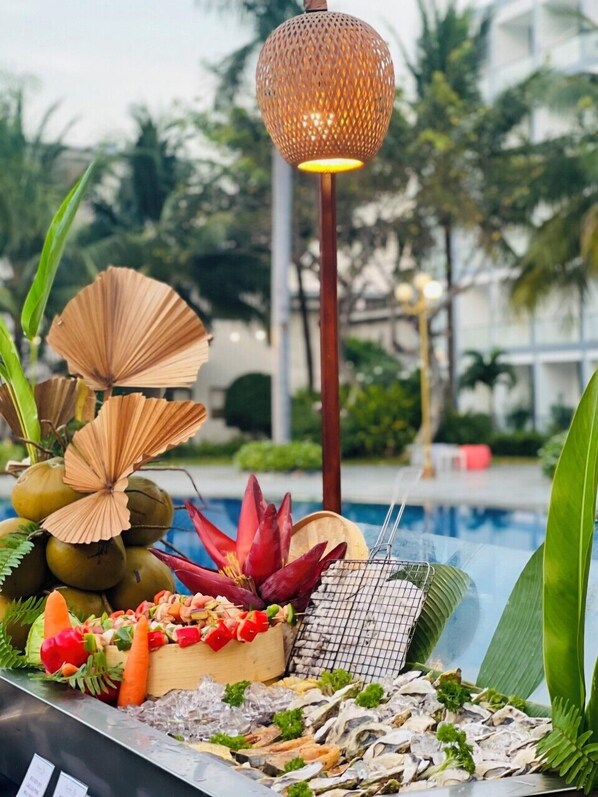 A poolside buffet with tropical decorations, a decorative lamp, and a variety of seafood and vegetables.