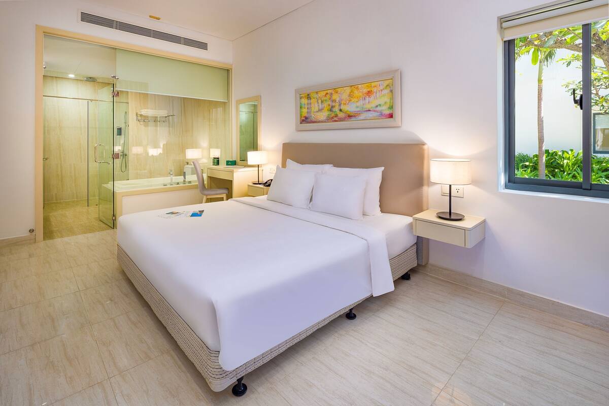 A hotel room with a bed, bedside table, lamp, and a window with a view.