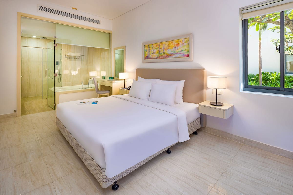 A hotel room with a bed, bedside tables, a desk, a shower area, and a window with a view.