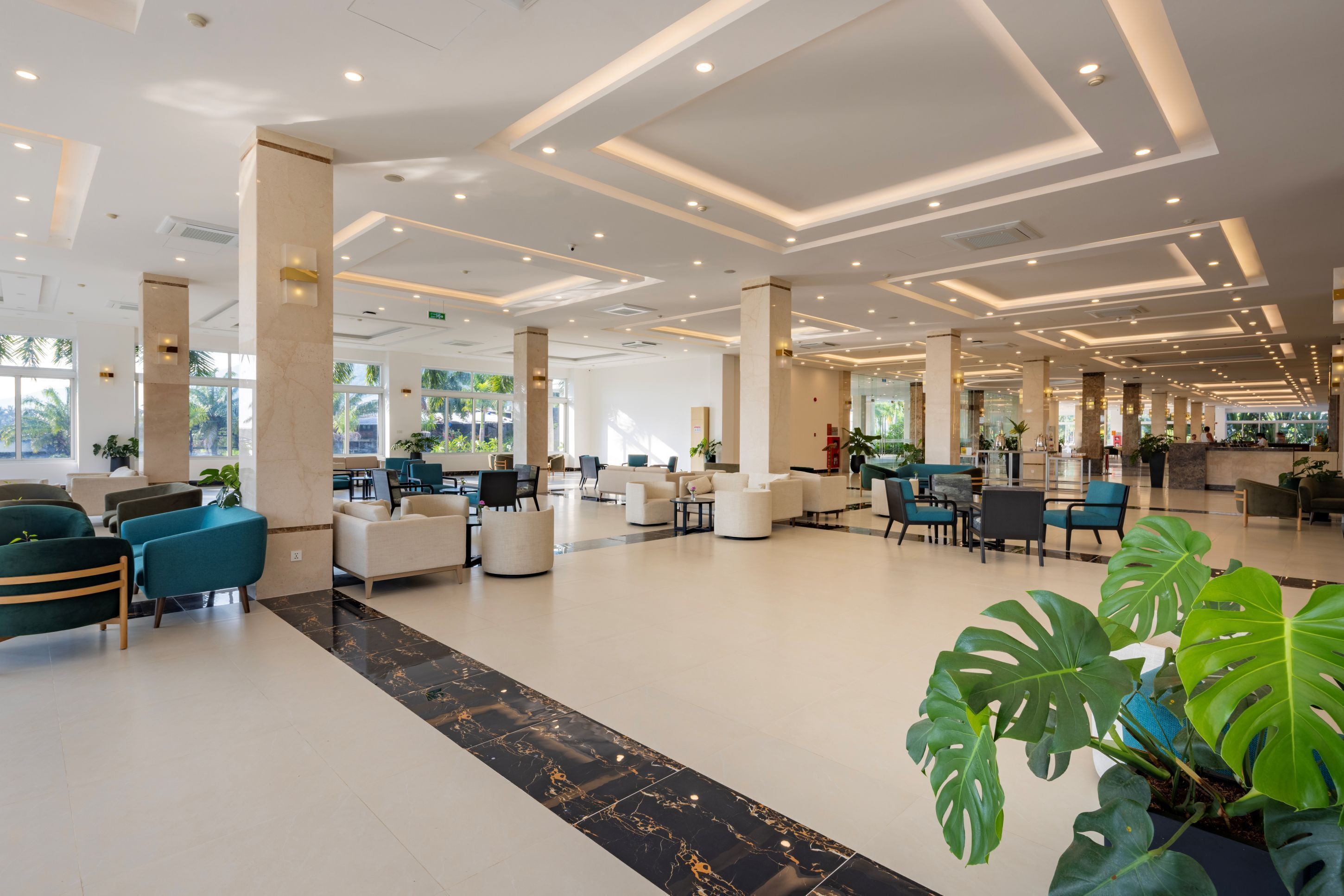 A spacious lobby with modern seating, large windows, and a central plant area.