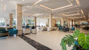 A spacious lobby with modern seating, large windows, and a central plant area.