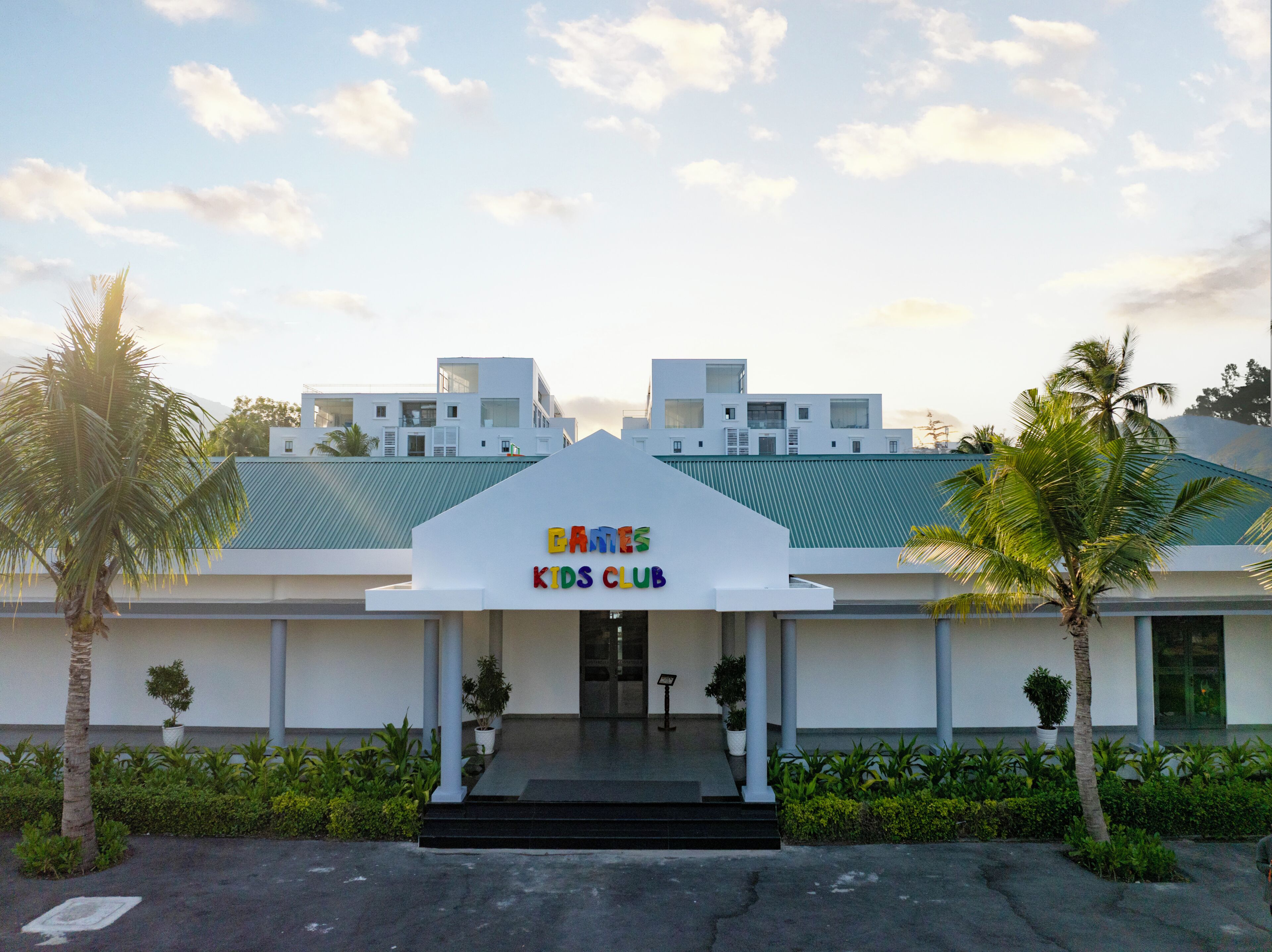 Ein Gebäude mit einem Schild, auf dem 'BAMES KIDS CLUB' steht, und moderner Architektur mit flachem Dach und weißer Fassade.