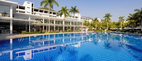 A swimming pool with a tiled floor, surrounded by a building with multiple balconies and palm trees.