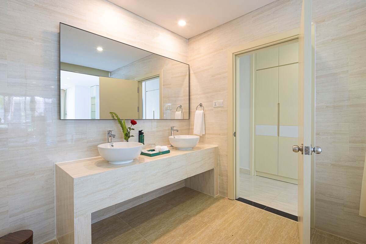 A modern bathroom with a large mirror, two sinks, a towel rack, and a door.