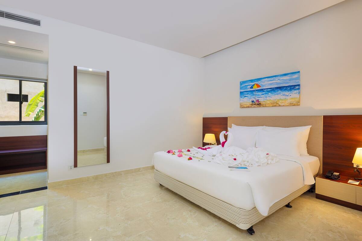 A hotel room with a bed, a nightstand, a lamp, a painting, and a mirror.