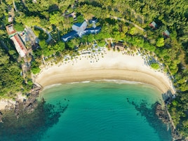 Vista aérea de una playa con una costa curvada, rodeada de abundante vegetación y algunos edificios.