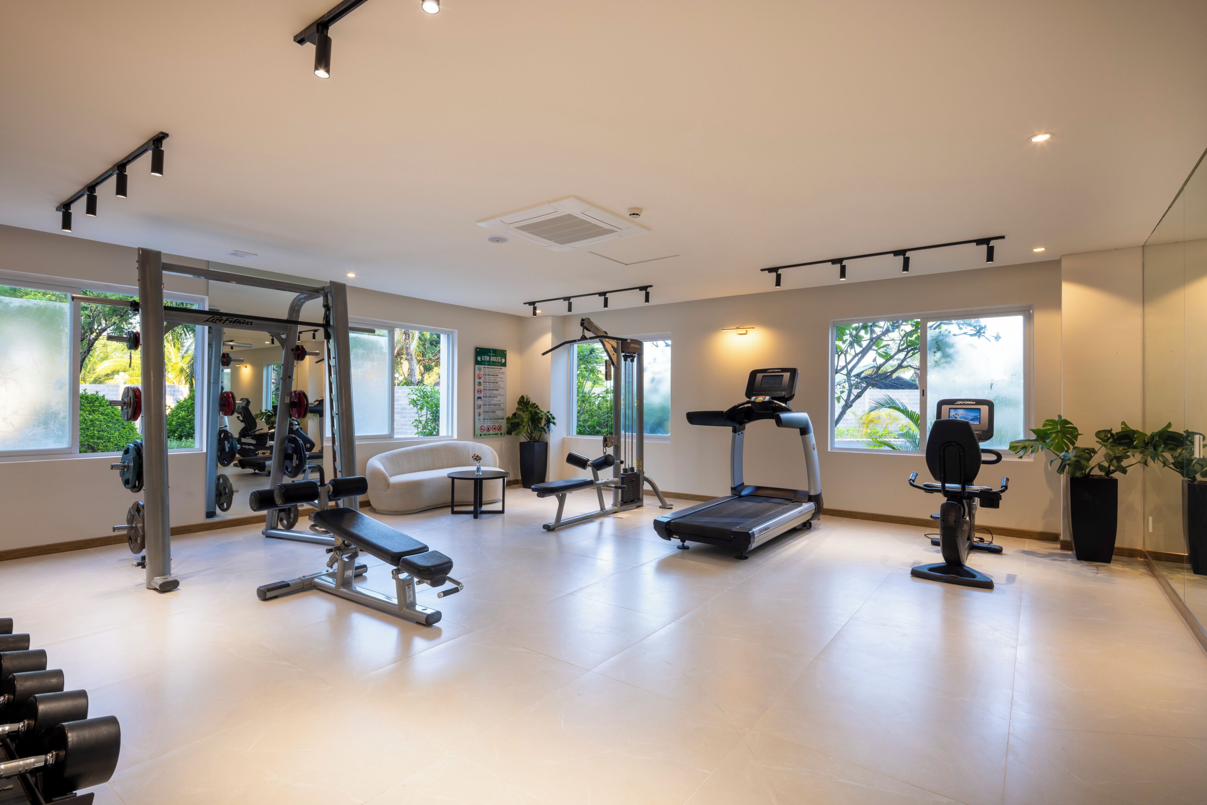 A modern gym with various exercise equipment, large windows, and a clean, spacious layout.