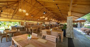 Un restaurante espacioso con mesas y sillas de madera, un pilar de piedra y luminarias colgantes.