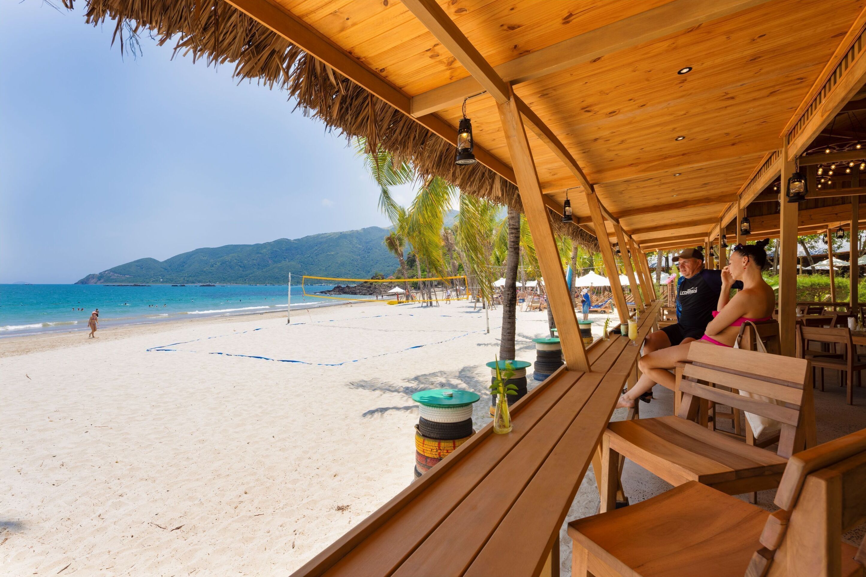 A beachside wooden structure with benches, a volleyball net, and a view of the beach and ocean.