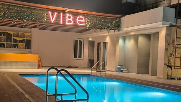 A swimming pool area with a neon sign reading "VIBE" at night. - Coconut Lagoon Agro Resort (Parbhani)