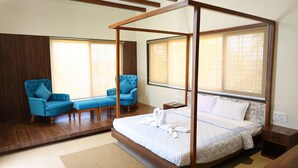 A bedroom with a four-poster bed, two blue armchairs, a wooden floor, and large windows with blinds. - Coconut Lagoon Agro Resort (Parbhani)
