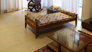 A spacious room with a large bed, a rocking chair, a glass-top coffee table, and a view of a balcony through sheer curtains. - Coconut Lagoon Agro Resort (Parbhani)