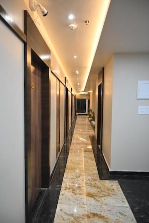 A long, narrow hallway with a polished marble floor, recessed lighting, and doors on both sides. - Sainik Grand (Varanasi)
