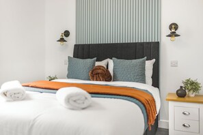 A neatly made bed with white and orange bedding, a dark headboard, and two wall-mounted light fixtures. - Aurum House (Blackpool)