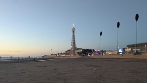 Una spiaggia con una torre imponente, un molo che si protende sull'acqua e un edificio con insegne illuminate.