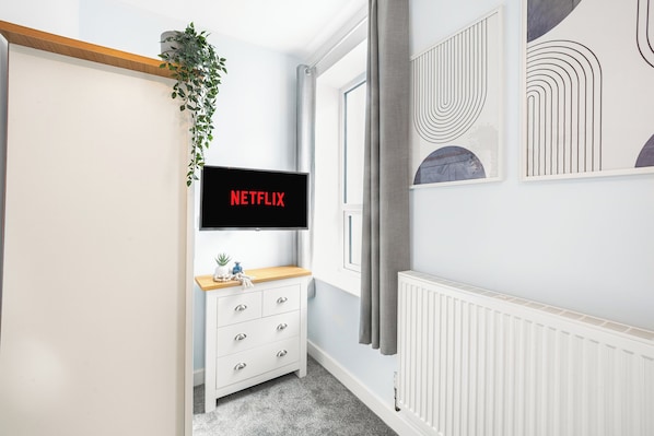 Une chambre moderne dotée d’un téléviseur à écran plat fixé au mur, d’une commode blanche avec des tiroirs, d’une petite plante et d’œuvres d’art abstraites accrochées au mur.