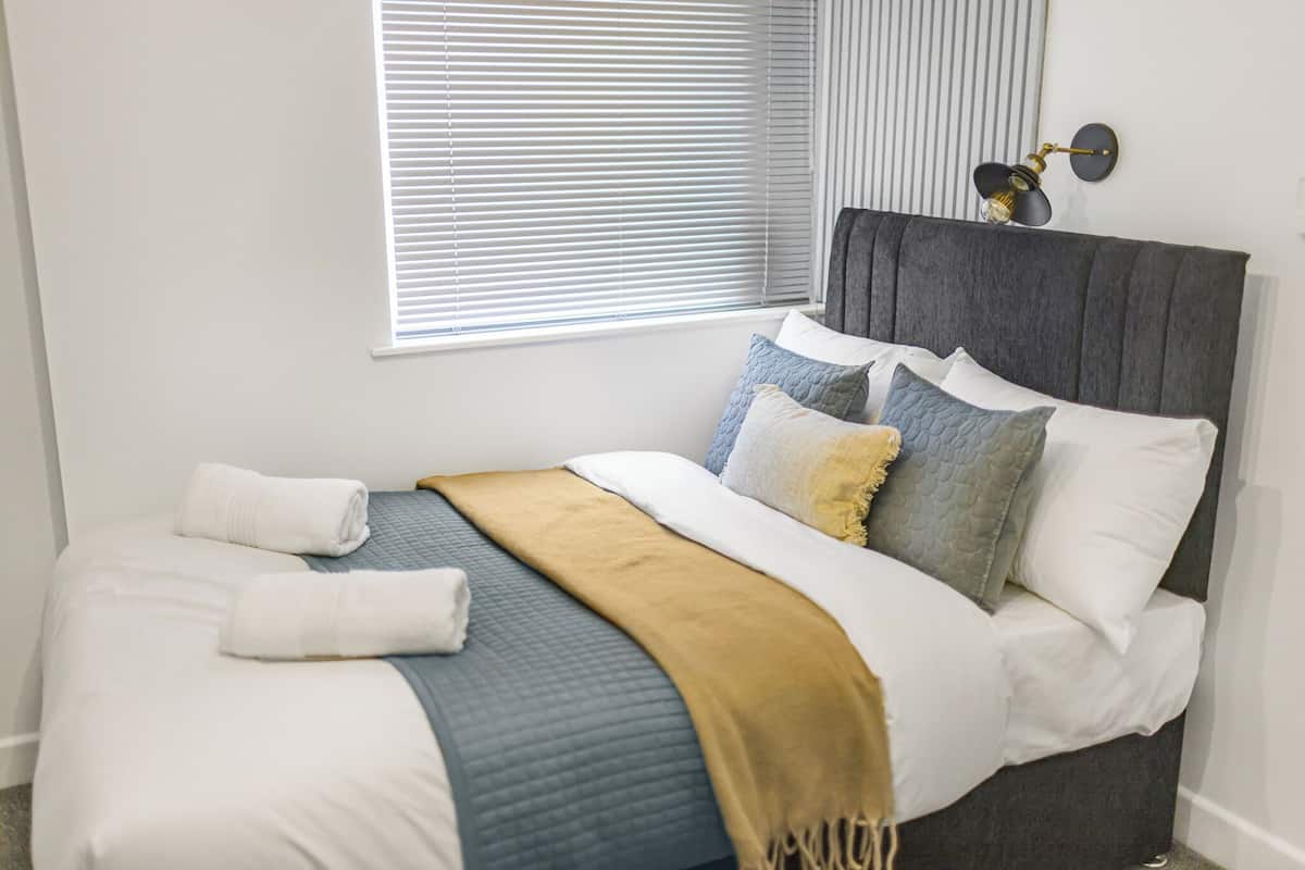 A neatly made bed with a grey headboard, white and blue bedding, and a mustard-colored throw blanket.