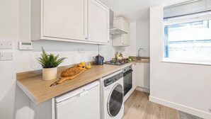 Una cucina moderna con mobili bianchi, un piano di lavoro in legno, una lavatrice e una finestra con persiane.