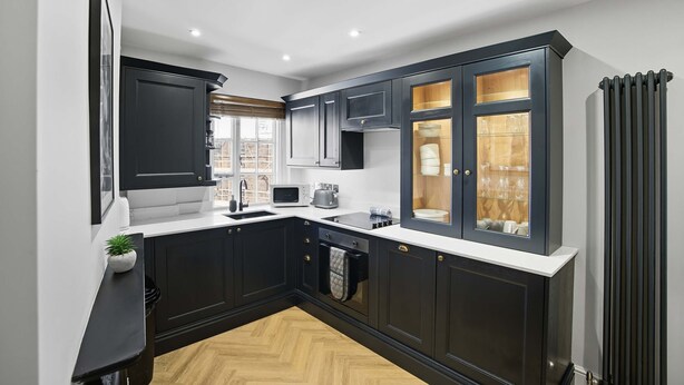 A compact kitchen with dark cabinetry, a white countertop, and a visible window. - Aldwark Mews (York)