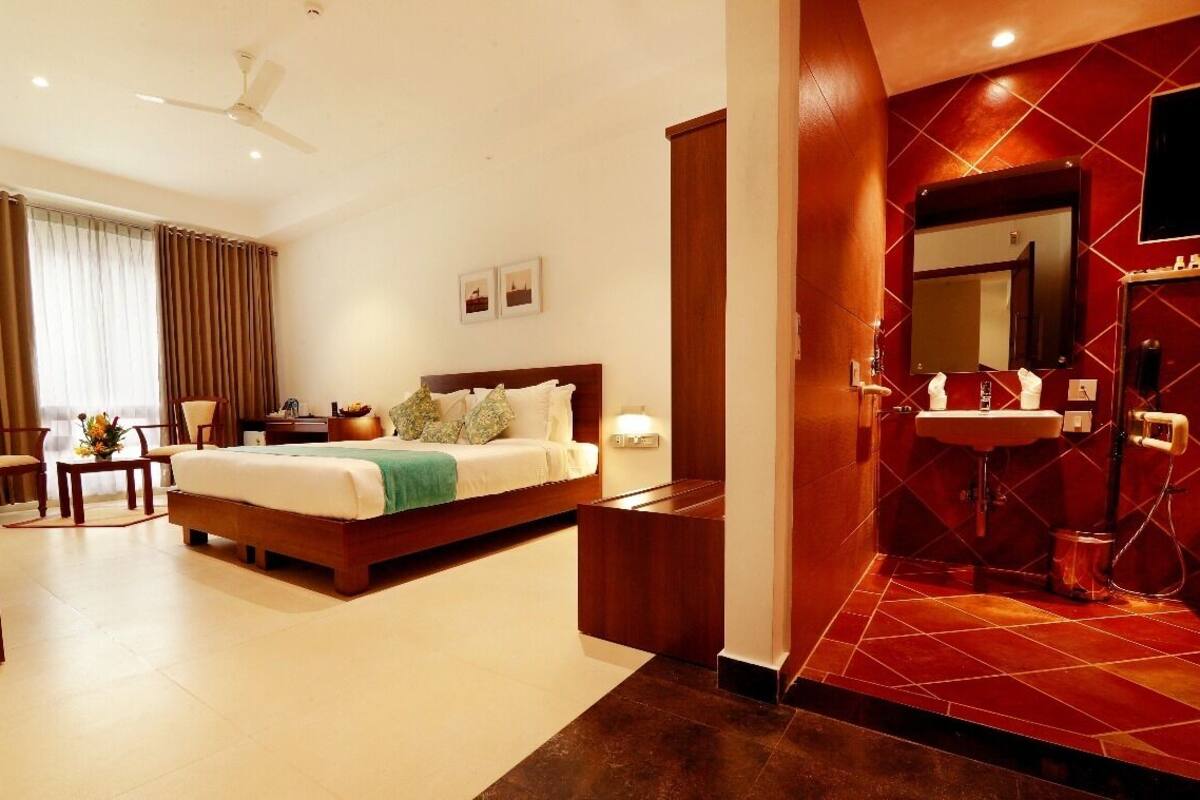 Een hotelkamer met een bed, een bureau, een stoel, een kleine tafel met bloemen, een spiegel en een badkamer met rode tegels.