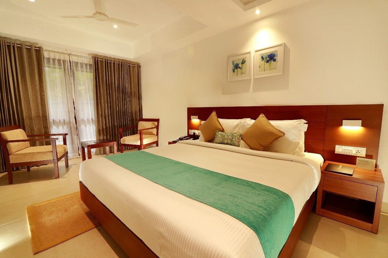 A hotel room with a large bed, a wooden nightstand, a chair, a desk, and a ceiling fan.