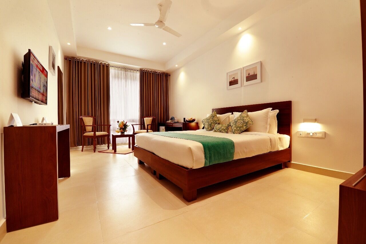Quarto de hotel com uma cama grande, uma escrivaninha, uma cadeira, uma televisão e cortinas.