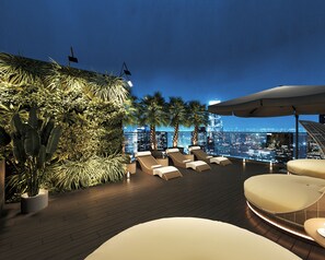 Un salon sur le toit, doté de fauteuils confortables et offrant une vue sur les lumières de la ville la nuit.