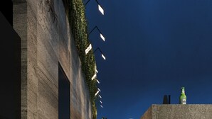 A modern building exterior with a stone facade, a staircase, and a small outdoor seating area with a bottle and umbrella. - L'Heritage Premium Hanoi Central (Hanoi)