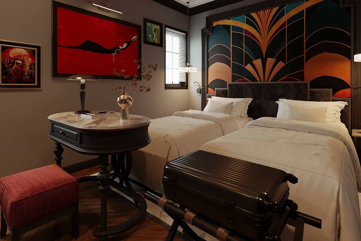 Een hotelkamer met twee bedden, een bureau, een rode bank, een koffer en een bijzondere plafondlamp.