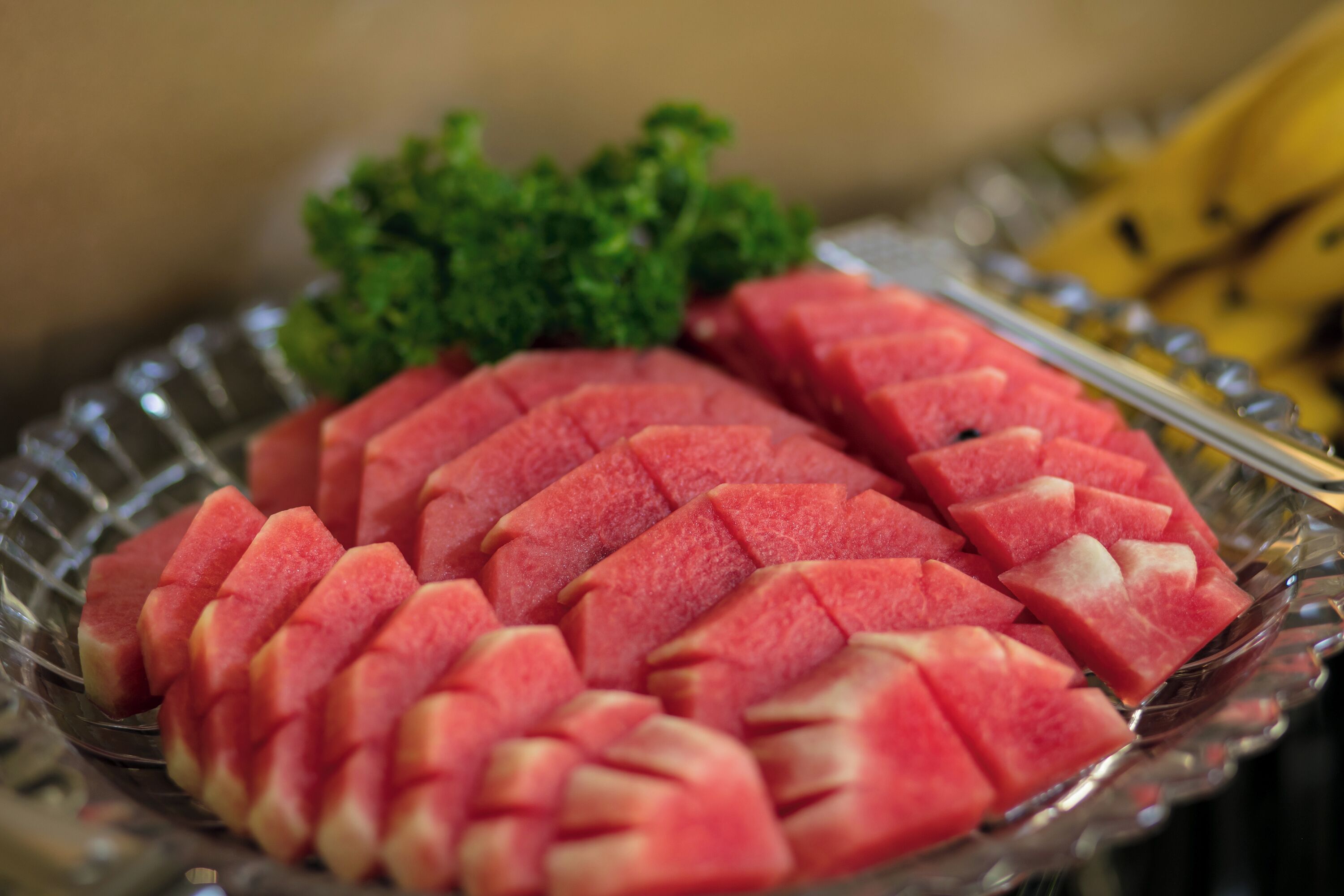 A glass dish with neatly arranged watermelon slices and a green garnish.