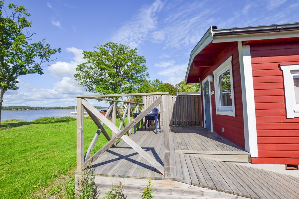A red cabin with a wooden deck overlooking a lake.