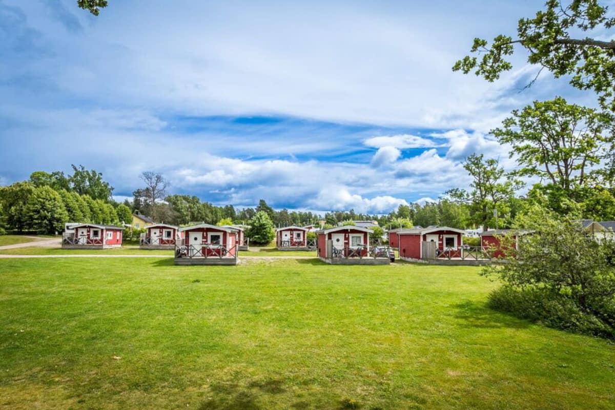 Une rangée de maisons mobiles rouges, avec un champ verdoyant au premier plan et des arbres en arrière-plan.