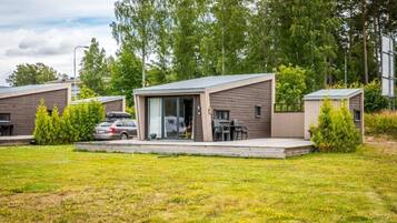 A modern RV-style accommodation with a covered patio, a carport, and a grassy lawn.