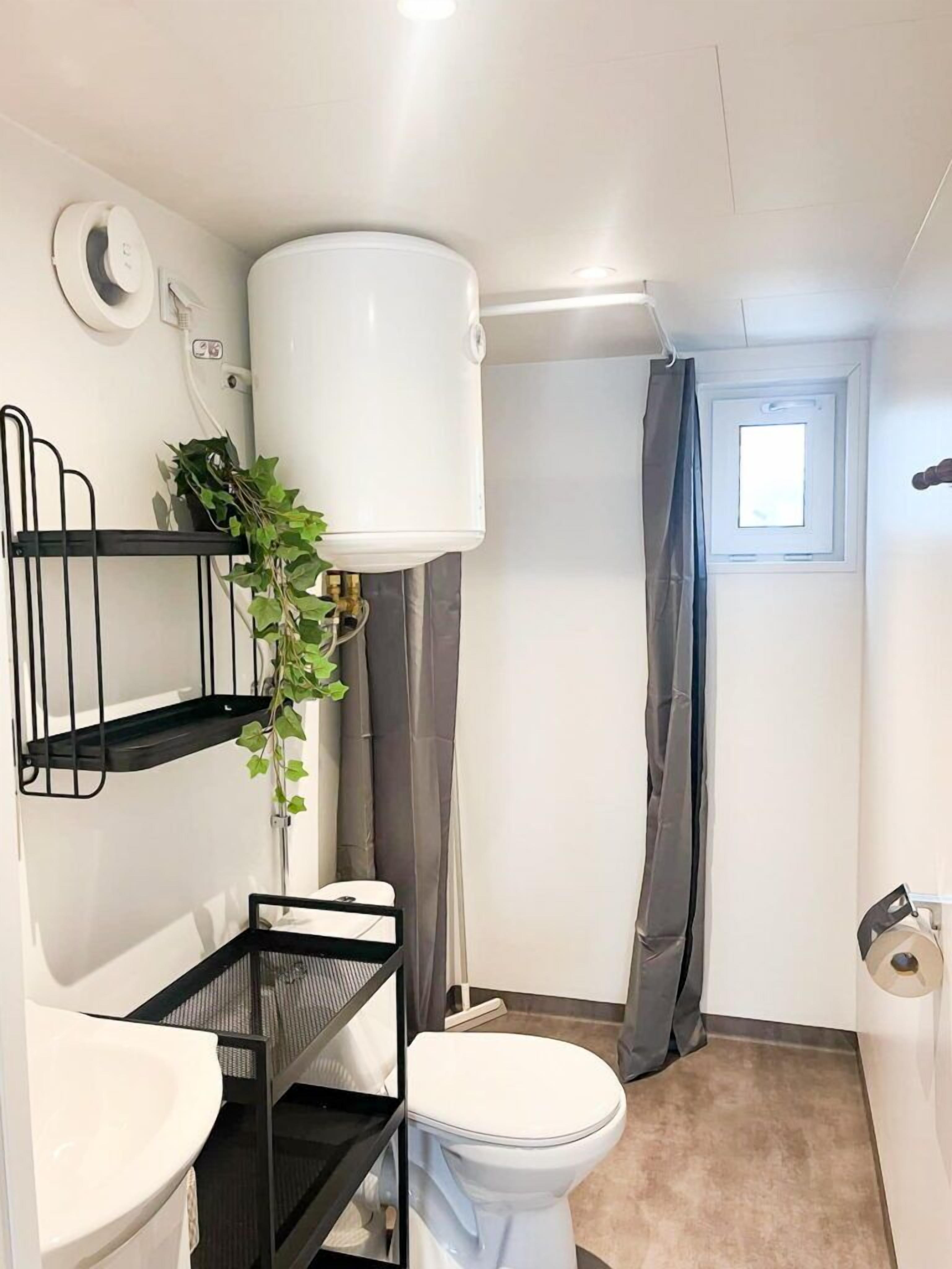 Um banheiro compacto com vaso sanitário, pia e aquecedor de água branco fixado na parede.