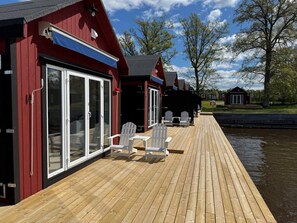 A wooden deck with white chairs and a table, leading to a red building with glass doors. - First Camp Herrgårdsliv - Kristinehamn (Kristinehamn)