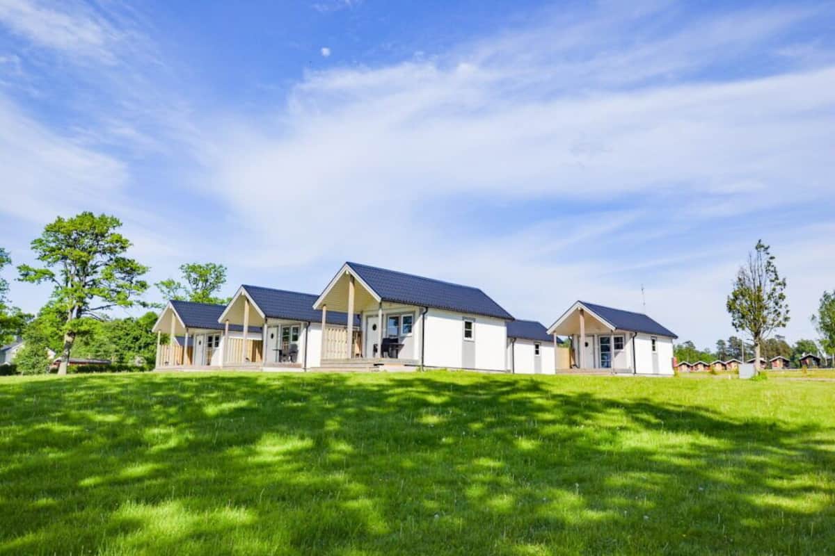 Une rangée de trois maisons de plain-pied, avec des toits sombres, des murs blancs et une pelouse verdoyante à l’avant.