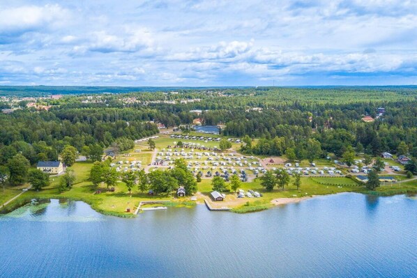 An aerial view of a lakeside campground with multiple RVs and cabins, surrounded by dense forest and a small dock. - First Camp Herrgårdsliv - Kristinehamn (Kristinehamn)