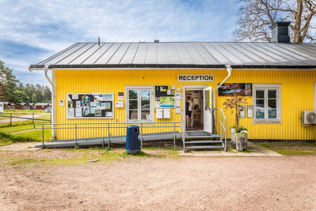 En gul byggnad med en reception, ett litet område med utomhusplatser och en soptunna.