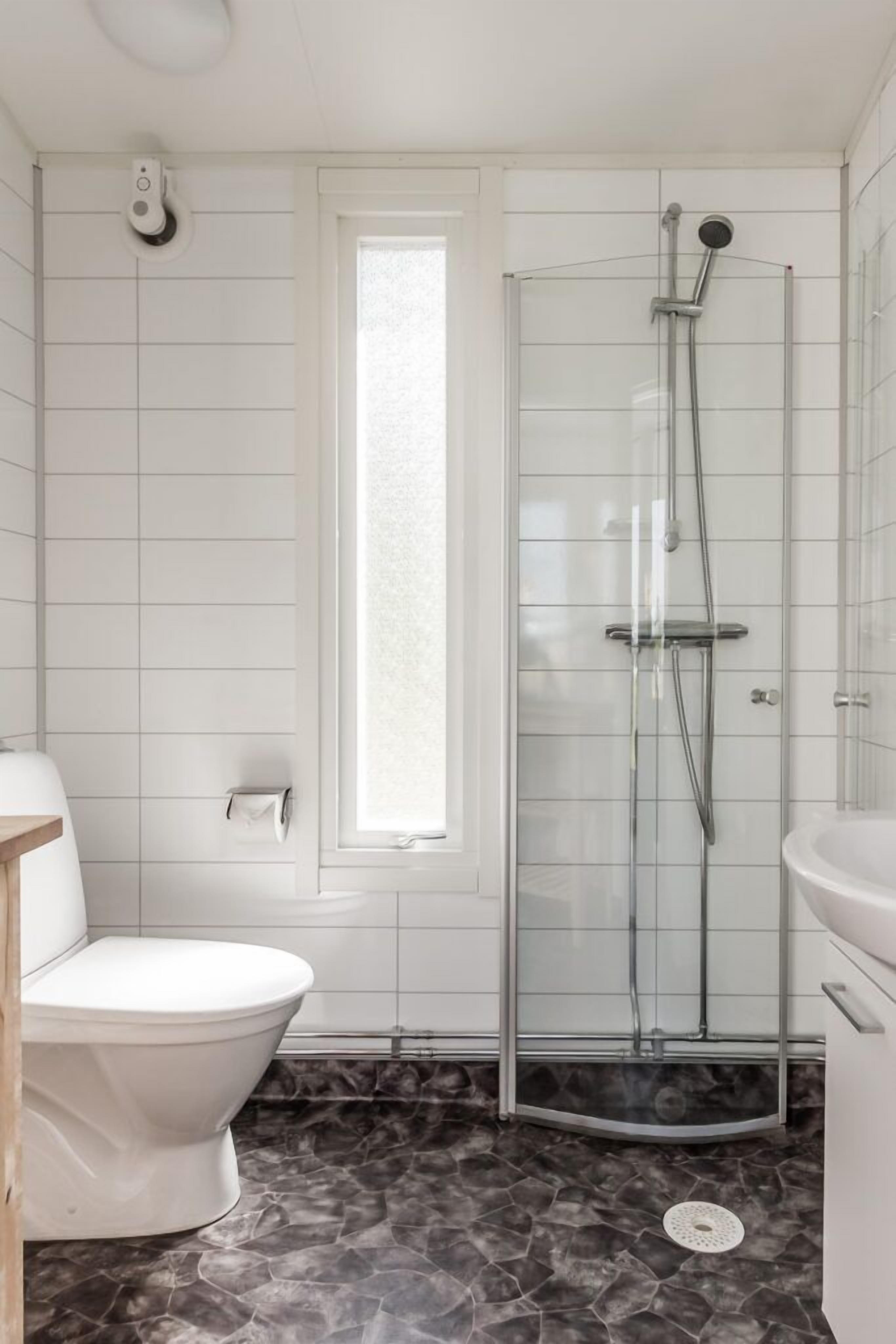 A bathroom with a toilet, a glass-enclosed shower, and a marble floor.