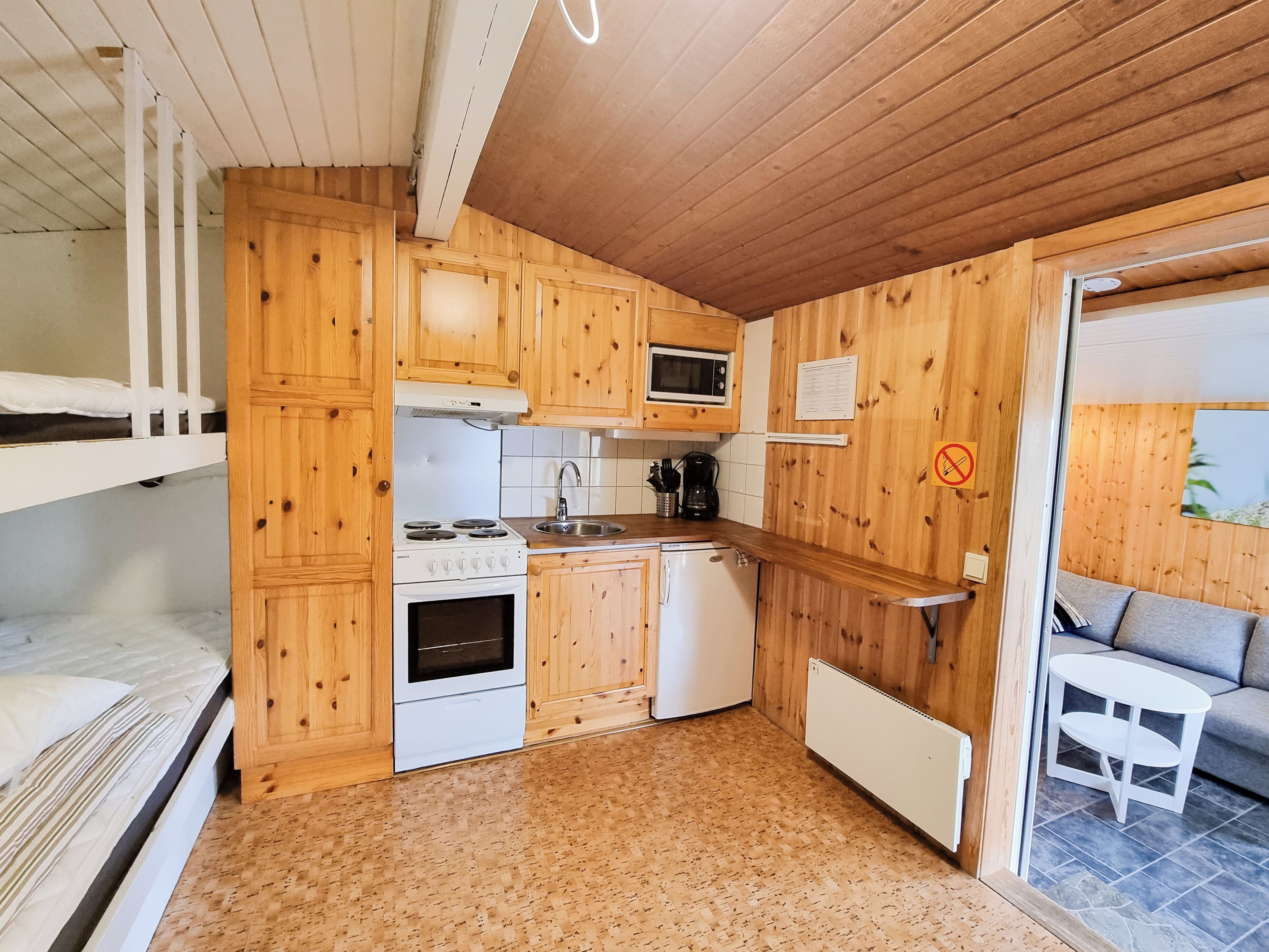A compact kitchen with wooden cabinets, a stove, microwave, and a small refrigerator.