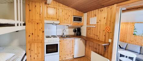 A compact kitchen with wooden cabinets, a stove, microwave, and a small refrigerator.