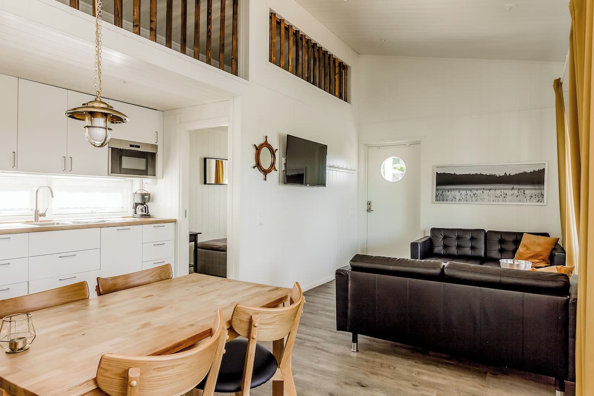 A modern kitchen with white cabinets, a wooden dining table, and a black leather sofa.