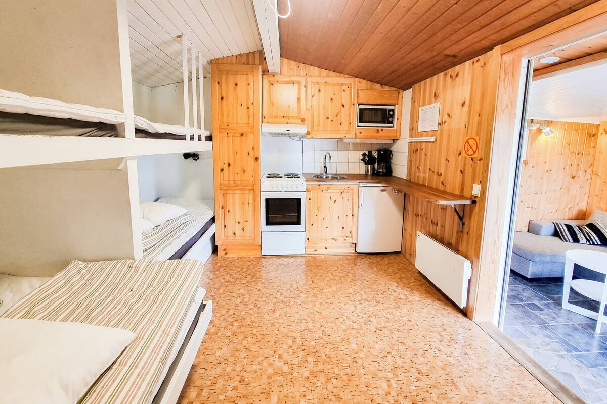A compact room with bunk beds, a kitchenette, and a small seating area.