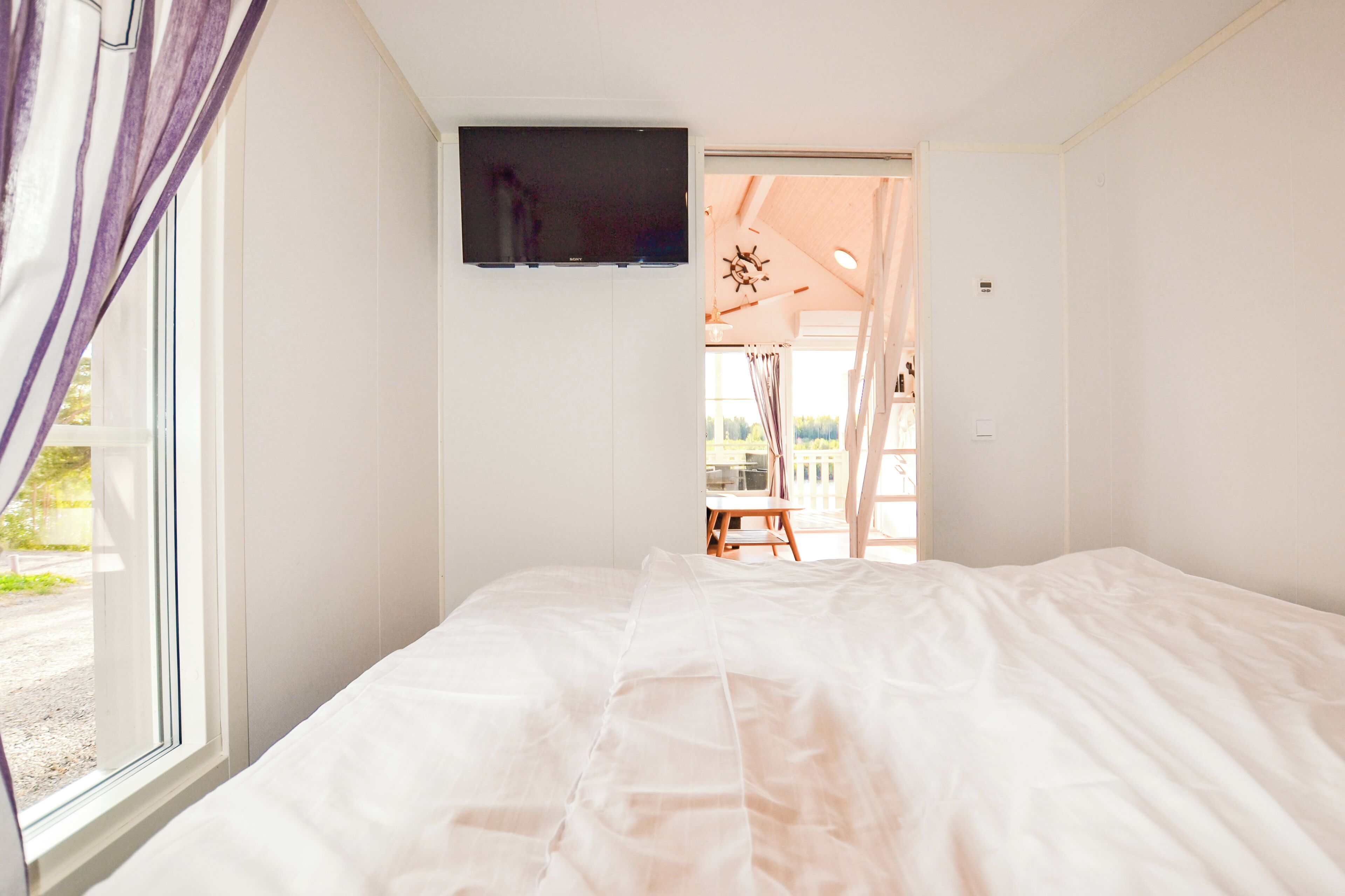 Un dormitorio con una cama, un televisor montado en la pared y una ventana con cortinas.